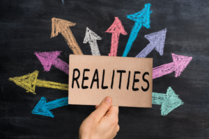 Hand holding up the sign, realities, and various arrows pointing in different directions, indicating the multiple realities that educators navigating burnout face and how to properly work toward congruency